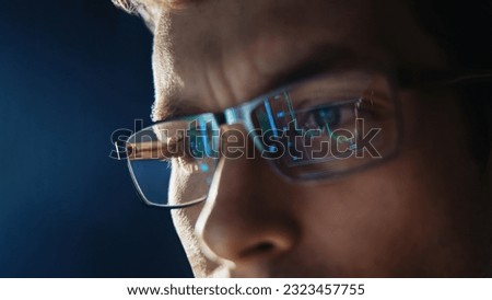 Close up view of focused trader wears eyeglasses looking at pc screen with stock market charts reflection, working online late night. Man analysing crypto market. Selective focus on eye. Copy space. 