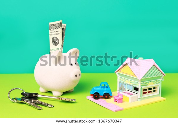 Close up view of \
four important object for  life. Piggy bank with one hundred\
dollars, keys for home, toy car and small cute toy house isolated\
on green and blue\
background
