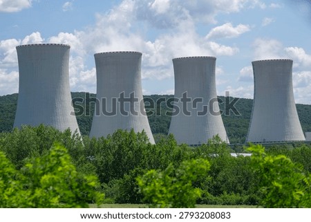 close up view of four massive concrete cooling towers of a nuclear power plant emitting white steam against a blue sky with clouds