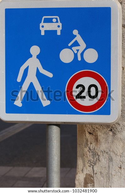 Close up view of a french traffic sign in a pedestrian\
street. Symbol indicating that the speed is limited at 20\
kilometers per hour for cars and cycles. Blue and white metallic\
sign, Urban image.  