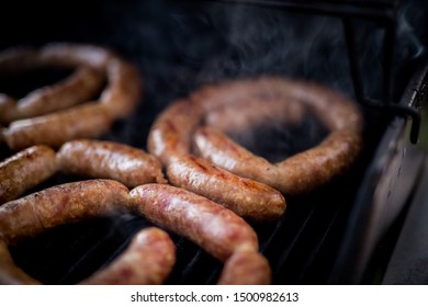 Close Up View Of Freshly Made Pork Sausage Links Cooking On The Barbecue Grill.  The Smoke Is Made From The Fat Dripping Into The Fire Below.