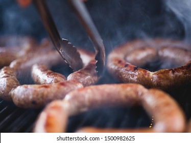 Close Up View Of Freshly Made Pork Sausage Links Cooking On The Barbecue Grill.  The Smoke Is Made From The Fat Dripping Into The Fire Below.