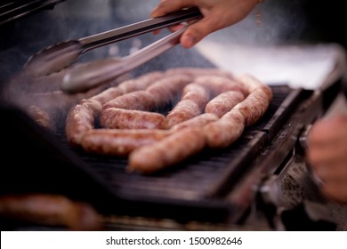 Close Up View Of Freshly Made Pork Sausage Links Cooking On The Barbecue Grill.  The Smoke Is Made From The Fat Dripping Into The Fire Below.