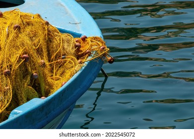 Close up view of the front of a moored blue wooden fishing boat with yellow nylon fishing nets with rope and floaters draped on the front of the boat in tranquil water of a Greek harbor