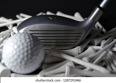 Close Up View Of A Golf Club Head On A Bed Of White Golf Tees And A Golf Ball In The Foreground.  Black Background With Dramatic Lighting.