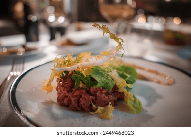 Close up view of gourmet dish in fine dining setting. Plate elegantly presented with finely chopped raw meat, greens, and yellow vegetable strands. Upscale restaurant atmosphere. - Powered by Shutterstock