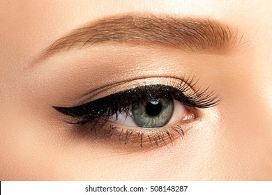 Close up view of gray woman eye with beautiful golden shades and black eyeliner makeup. Classic make up. Studio shot