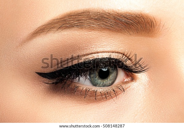 Close up\
view of gray woman eye with beautiful golden shades and black\
eyeliner makeup. Classic make up. Studio\
shot
