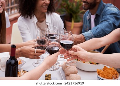 Close up view of a group of unrecognizable people toasting with red wine outdoors, having fun enjoying the day together with food and drinks. Multiracial friends gathering to celebrate. - Powered by Shutterstock