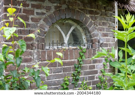 Close up view of half moon window in dilapidated and abandoned farmhouse with thatched roof in countryside the Netherlands with weeds, grasses growing in front
