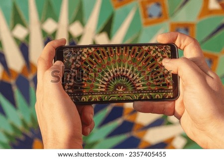 close up view of a hand holding a phone and taking a photo of a moroccan mosaic pattern at Hassan II mosque exterior - Casablanca, Morocco
