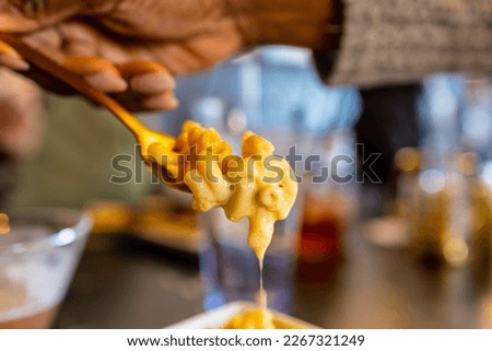 close up view of a hand picking up delicious mac and cheese with a fork. the cheese is dripping nicely from the silverware.  southern style homemade comfort food