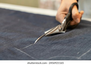 Close up view of hand with scissors cutting a fabric.