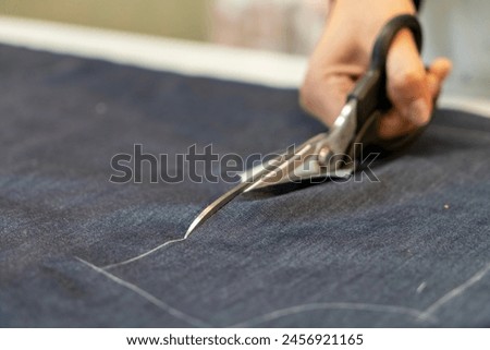 Close up view of hand with scissors cutting a fabric.