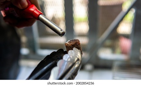 Close Up View Of Hand Using A Gas Lighter Starter To Ignite Camping Charcoal Cock Fire Starter For Barbeque Party.