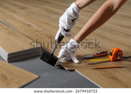 Close view of hands aligning SPC vinyl plank on acoustic underlayment with a rubber mallet and tools during flooring work