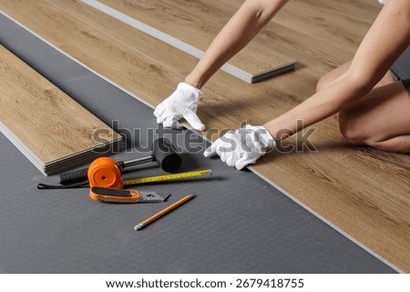 Close view of hands aligning SPC vinyl plank on underlayment with tools and tape for home renovation