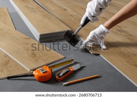 Close view of hands aligning SPC vinyl plank on acoustic underlayment with a rubber mallet and tools during flooring work