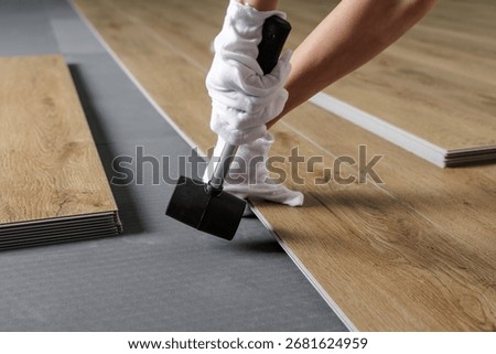 Close view of hands aligning SPC vinyl plank on acoustic underlayment with a rubber mallet during flooring installation