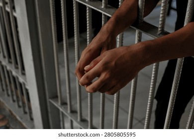 Close up view of hands behind bars in a prison cell, symbolizing incarceration and the criminal justice system.