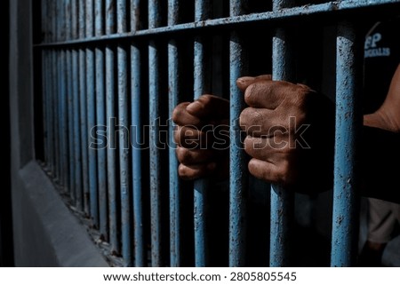 Close up view of hands behind bars in a prison cell, symbolizing incarceration and the criminal justice system.