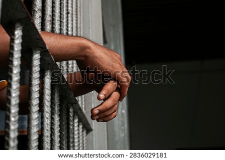 Close up view of hands behind bars in a prison cell, symbolizing incarceration and the criminal justice system.
