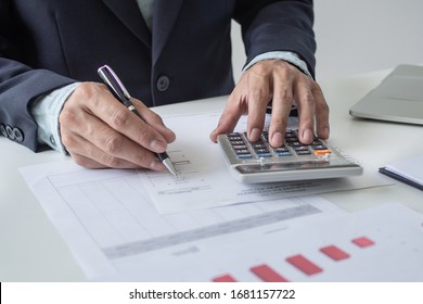 Close up view hands of businessman using calculator and doing accounting with graph and documents on the table.