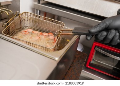 Close Up View Of The Hands Of A Chef Frying Frankfurts In An Industrial Fryer In A Kitchen