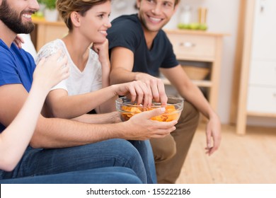 Close Up View Of The Hands Of A Group Of Young Friends Eating Snacks Digging Into A Bowl Of Potato Chips While Watching Television