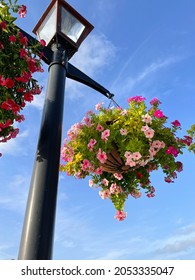 Close Up View Of Hanging Pot With Wild Flowers On The Street Lamp Post With Blue Sky On The Background