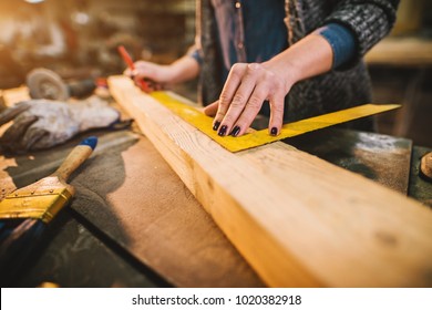 Close up view of hardworking focused professional serious carpenter woman holding ruler and pencil while making marks on the wood at the table in the fabric workshop. - Powered by Shutterstock