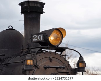 A Close Up View of the Headlight, Marker Light, and Smoke Dtack of Steam Locomotive 20 on a Cloudy Day