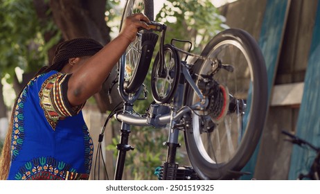 Close view of healthy african american lady meticulously inspecting and maintaining bicycle components. Female cyclist outdoors repairing bike crank arm and pedal for summer cycling. - Powered by Shutterstock