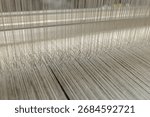 Close view of heddles and warp threads on a modern loom in a textile factory showing precision weaving and quality production