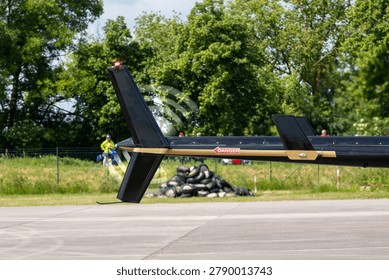Close view helicopter tail section spinning tail rotor above airfield pavement. Aviation engineering detail highlights safety markings, mechanical design and rotorcraft technology in outdoor setting