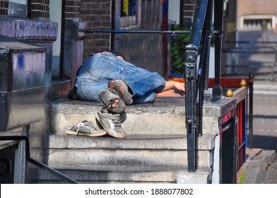 Close Up View Of A Homeless Person Sleeping On A Stoop Of A Canal House In Amsterdam, The Netherlands; Shoes Off And Holes Is His Socks Visible