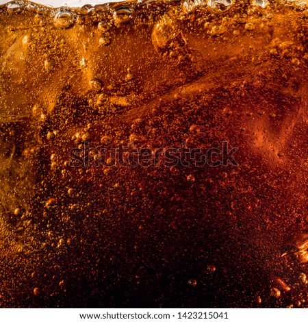 Close up view of the ice cubes in dark cola background. Texture of cooling sweet summer's drink with foam and macro bubbles on the glass wall. Fizzing or floating up to top of surface.