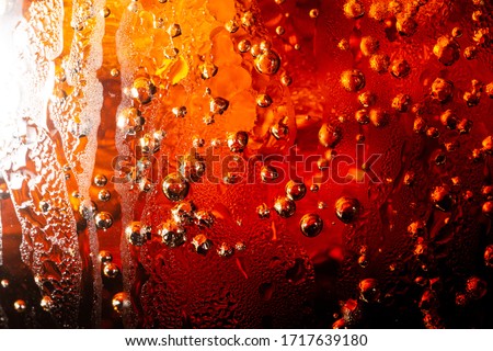 Close up view of the ice cubes in dark cola background. Texture of cooling sweet summer's drink with foam and macro bubbles on the glass wall. Fizzing or floating up to top of surface.