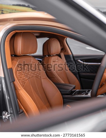 Close up view inside a modern car showing tan brown leather seats and polished controls