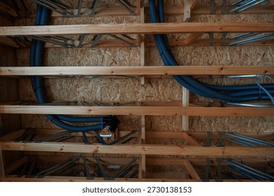 Close view inside shows OSB sheathing, solid joists, metal web trusses carrying blue corrugated ventilation ducts and conduit toward a distribution box during daylight rough in.