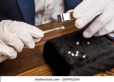 Close up view of jewelry appraiser examining gemstone in tweezers with magnifying glass at table