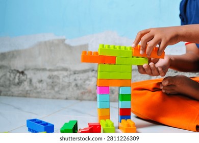 Close up view of a kid playing and stacking colorful plastic toy building blocks on the floor, focusing on fine motor skills development and screen-free creative activity.