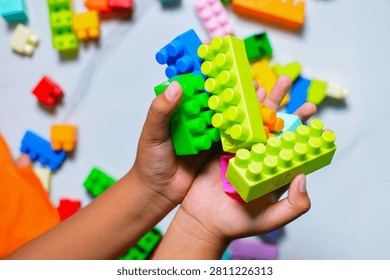 Close up view of a kid playing and stacking colorful plastic toy building blocks on the floor, focusing on fine motor skills development and screen-free creative activity.