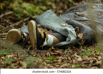 Close Up View Of Legs Of Dead Body Wrapped In Plastic Fabric Thrown In Woods Covered With Leaves