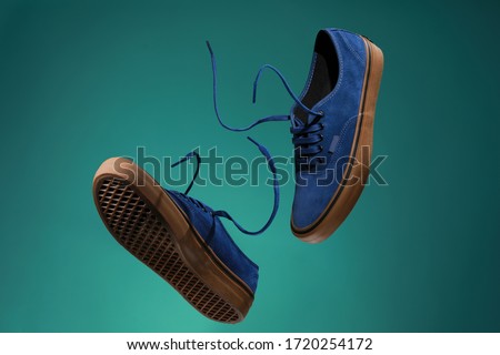 Close up view of levitation blue sneakers shoes with  flying laces over green background with copy space for text. 