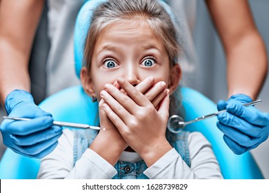 Close up view of a little girl looking scared and terrified screaming covering her mouth from the dentists with medical tools. Front view - Powered by Shutterstock