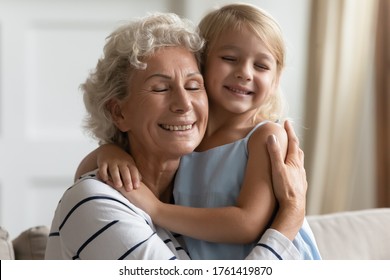 Close Up View Loving Grandmother Cuddle Snuggle To Small Granddaughter People Closed Eyes Enjoy Tender Moment Express Cherish And Sincere Affection, Sit On Sofa In Living Room, Love Protection Concept