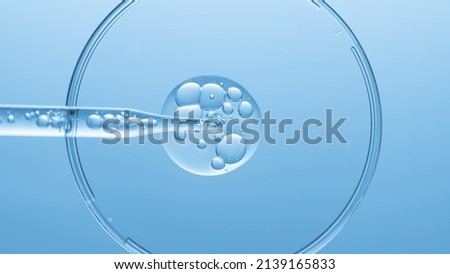 Close up view macro shot of gel with different sized bubbles comes out from lab dropper into petri dish on blue background | Abstract face care gel with hyaluronic acid mixing concept