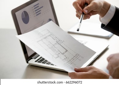 Close up view of male hand holding project plan, financial statistics data on laptop screen at background, analyzing real estate market, mortgage loan with low rate, construction investment - Powered by Shutterstock