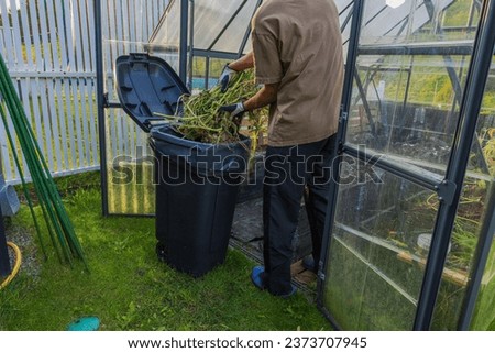 Close up view of man disposing of collected plants in trash, preparing greenhouse for winter season. Sweden.